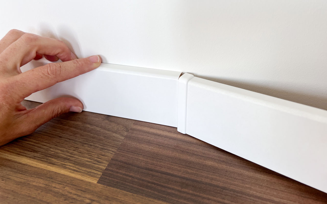 Montage von Sockelleisten: weiße MDF-Fußleisten werden mit Verbindungsstück an der Wand zusammengeführt