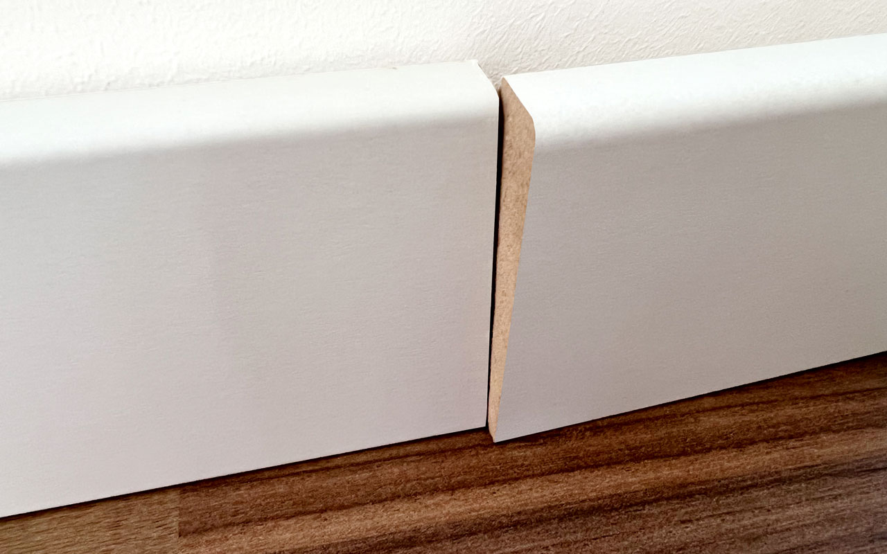 Zwei aneinanderstoßende MDF-Sockelleisten mit sichtbarem Höhenversatz vor dem Ausbessern.