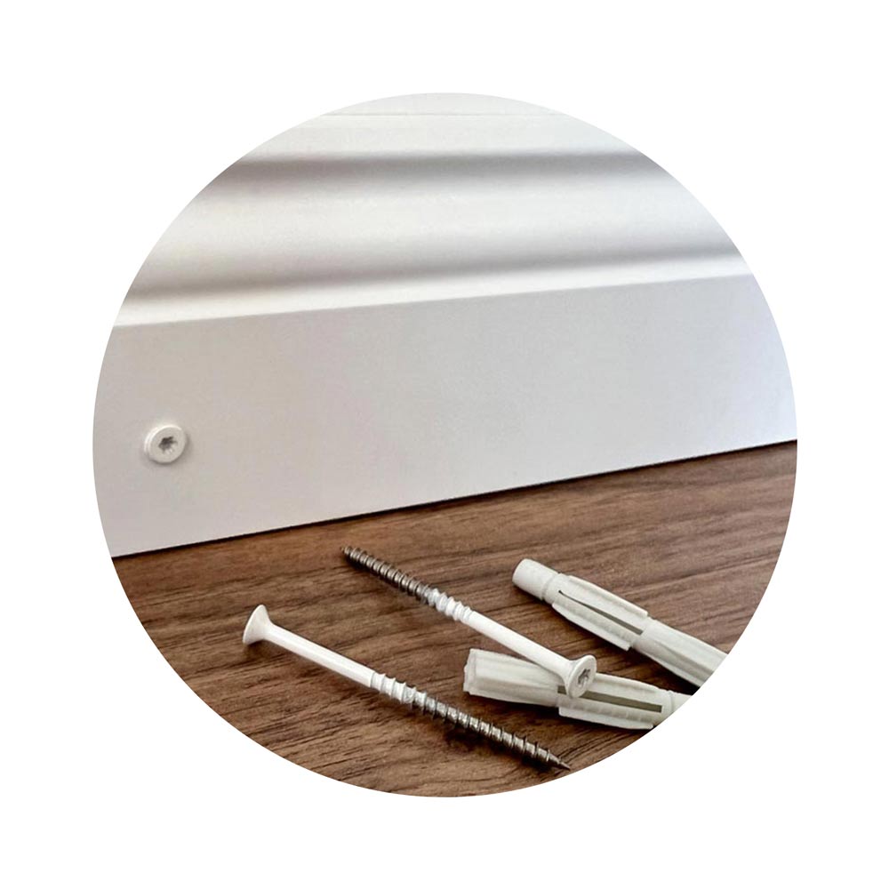 Schrauben und Dübel liegen vor einer weißen Sockelleiste