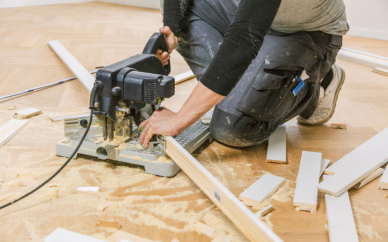 Handwerker kniet am Boden und schneidet Sockelleisten mit einer Kappsäge für passgenaue Montage.