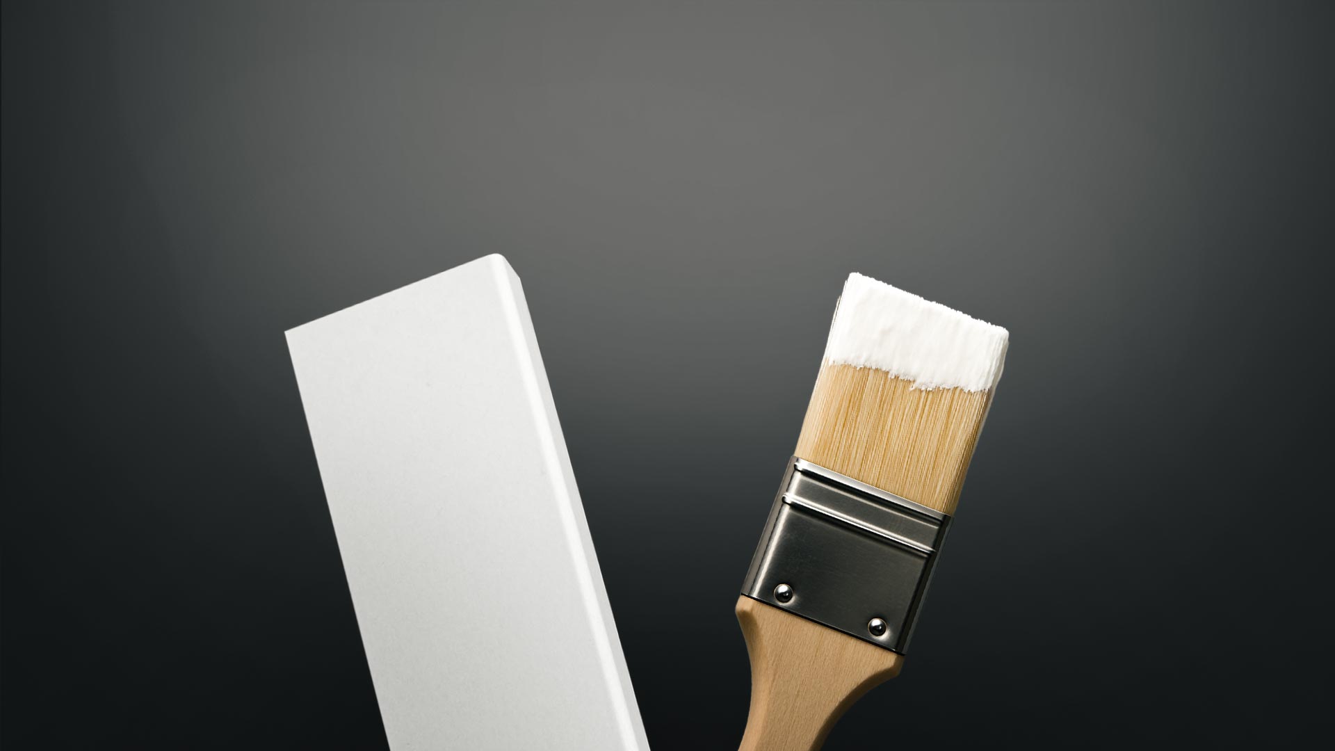 Weiße Sockelleiste neben einem mit weißer Farbe benetzten Flachpinsel vor dunklem Hintergrund