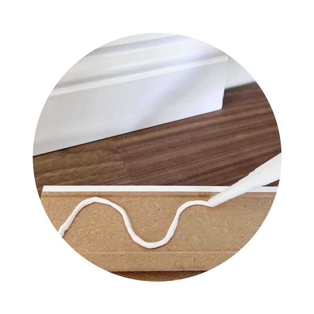 Sockelleiste wird mit weißem Montagekleber für die Montage an die Wand vorbereitet